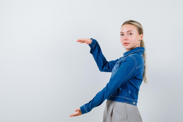 Chica joven que muestra algo gesto de mano grande sobre fondo blanco.