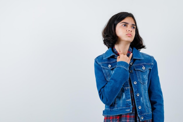 Chica joven que muestra el dedo meñique mientras mira a otro lado en camisa a cuadros y chaqueta de mezclilla y mira pensativa. vista frontal.
