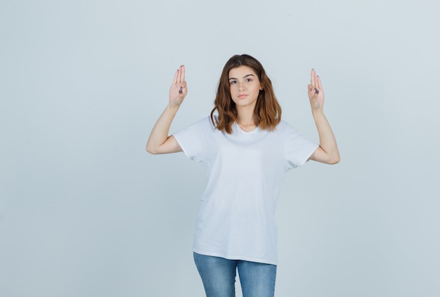 Chica joven que muestra un gesto aceptable en camiseta blanca, jeans y parece seguro. vista frontal.