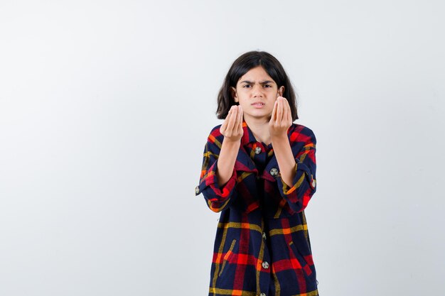 Chica joven que muestra gestos italianos en camisa a cuadros y parece serio. vista frontal.