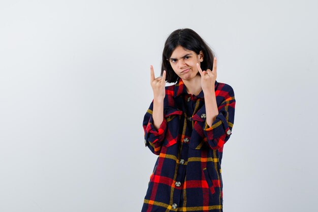 Chica joven que muestra gestos de rock n roll en camisa a cuadros y se ve linda. vista frontal.