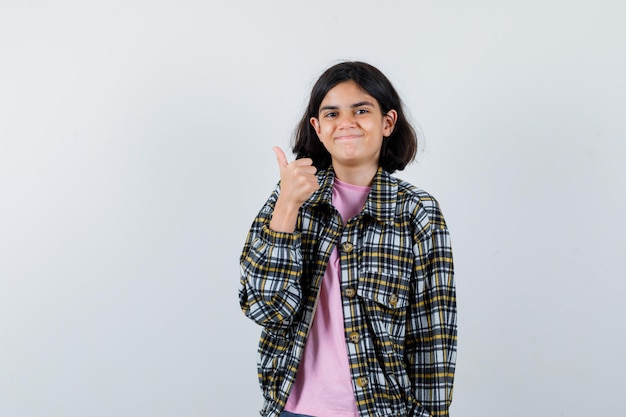 Chica joven que muestra el pulgar hacia arriba en camisa a cuadros y camiseta rosa y parece feliz. vista frontal.