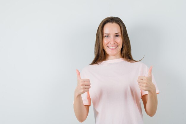 Chica joven que muestra los pulgares dobles para arriba en camiseta rosada y que parece alegre. vista frontal.