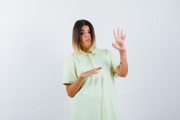 Chica joven que muestra la señal de pare, estirando una mano a un lado en la camiseta y mirando enfocado, vista frontal.