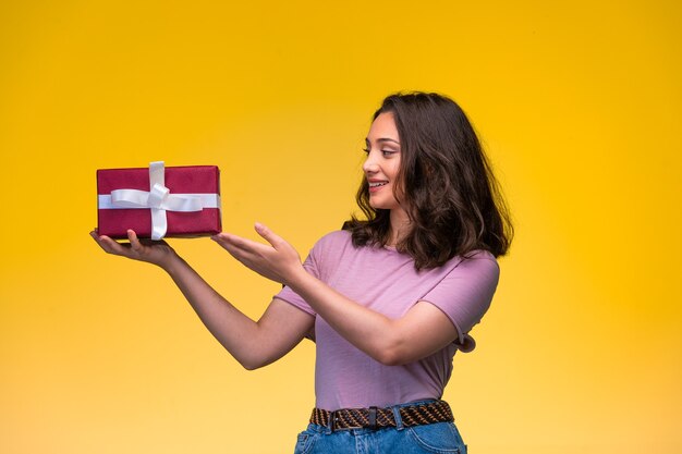 Chica joven que ofrece una caja de regalo roja y sonriente, vista de perfil.