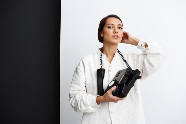 Chica joven que sostiene el teléfono viejo sobre la pared blanco y negro