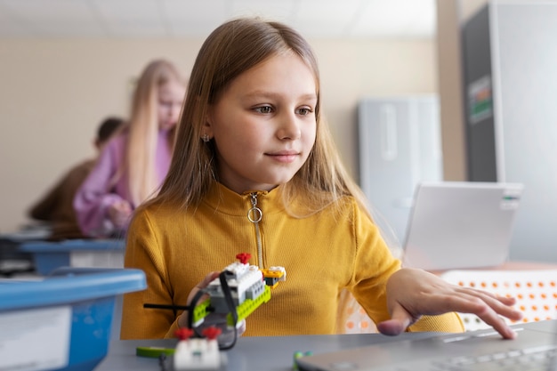 Chica joven que usa una computadora portátil y piezas electrónicas para construir un robot