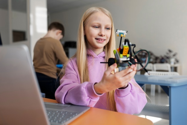 Chica joven que usa una computadora portátil y piezas electrónicas para construir un robot