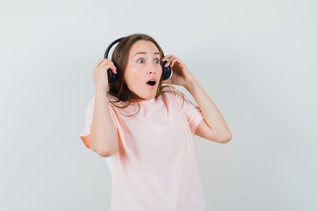 Chica joven quitándose los auriculares en camiseta rosa y mirando sorprendido