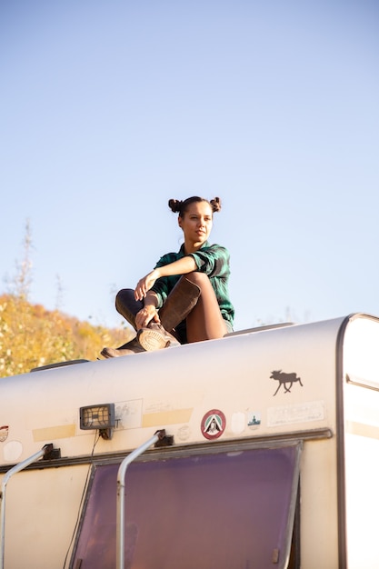 Chica joven relajándose en el techo de una autocaravana retro. Aventura en la naturaleza