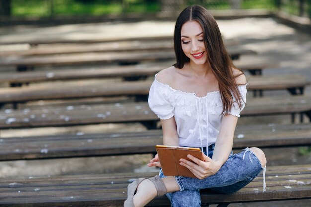 Chica jóven sentada en un banco de madera con una tablet