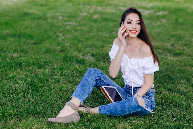 Chica joven sentada en un parque hablando por teléfono mientras sonrie