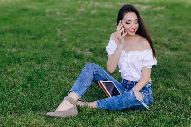 Chica joven sentada en un parque hablando por teléfono