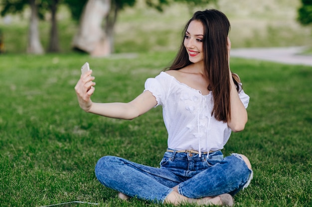 Chica joven sentada en un parque haciéndose una autofoto mientras sonrie