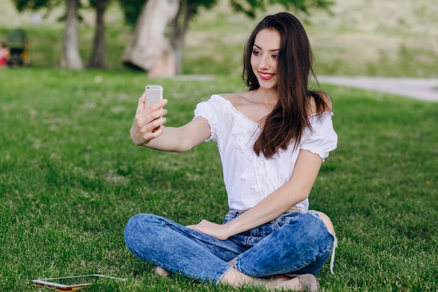 Chica joven sentada en un parque haciéndose una autofoto