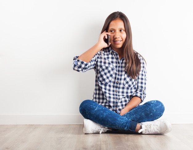 Chica joven sentada en el suelo hablando por teléfono