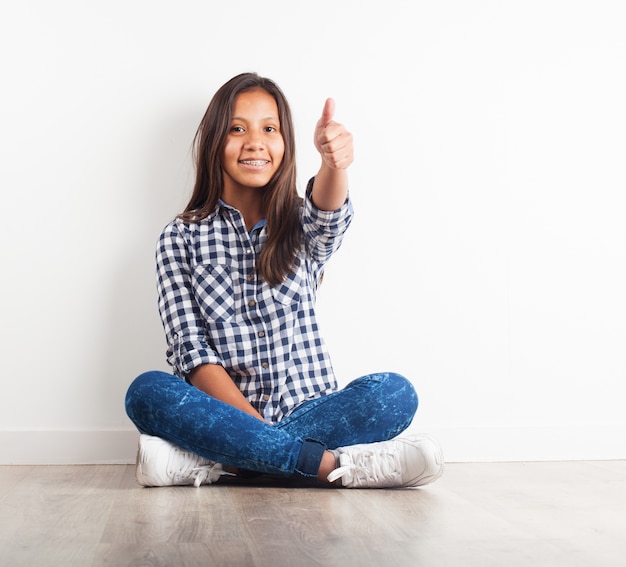 Chica joven sentada en el suelo sonriendo con un pulgar arriba