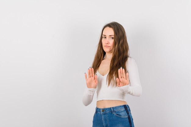 Una chica joven en serio está mostrando un gesto de parada con las manos en el fondo blanco