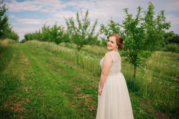 Chica joven con sobrepeso en vestido beige plantea jardín de primavera de fondo