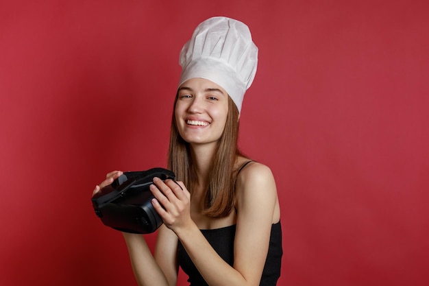 Chica joven con sombrero de chef y sosteniendo VR en fondo rojo