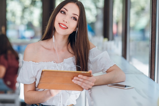 Chica joven sonriendo con auriculares y una tablet