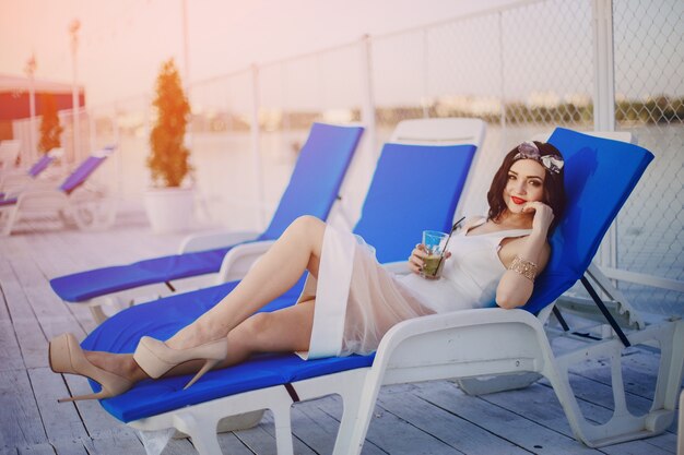 Chica joven sonriendo y tomando una bebida mientras está tumbada en una hamaca azul