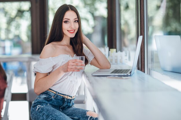 Chica jóven sonriendo con un vaso en la mano y un portátil al lado