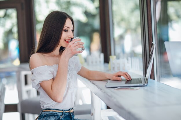 Chica jóven sonriendo con un vaso en la mano y un portátil al lado