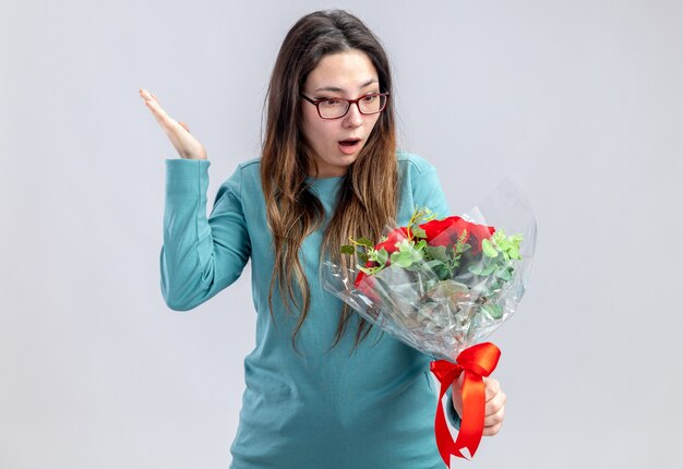 Chica joven sorprendida en el día de San Valentín sosteniendo y mirando el ramo extendiendo la cabeza aislada sobre fondo blanco