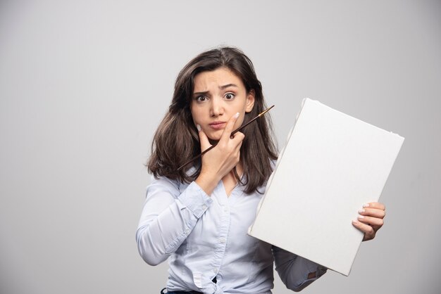 Chica joven sosteniendo un lienzo vacío y pensando en algo.