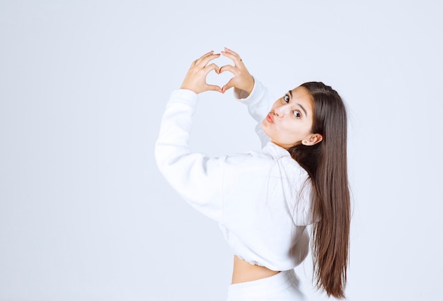 chica joven en sudadera con capucha blanca que muestra el corazón con las dos manos.