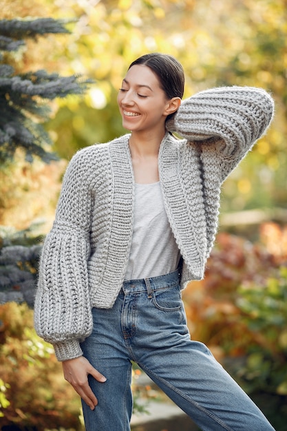 Foto gratuita chica joven en un suéter gris posando al aire libre