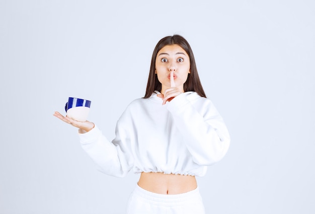 chica joven con una taza que muestra el signo de silencio.