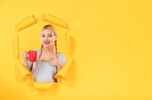 Chica joven con taza de té en compras faciales de fondo de papel amarillo rasgado