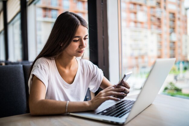 Chica joven con teléfono celular, computadora portátil y una taza de café