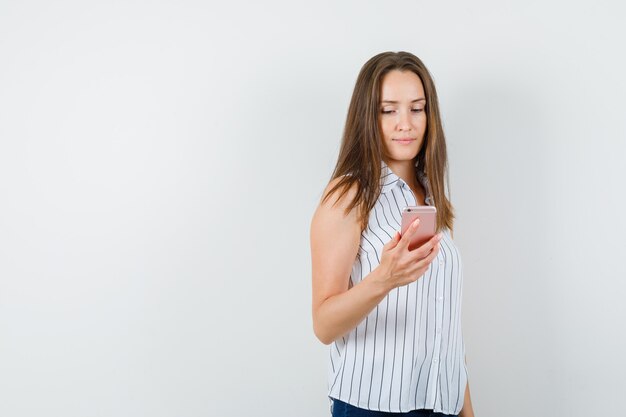 Chica joven con teléfono móvil en camiseta, jeans y mirando ocupado. vista frontal.