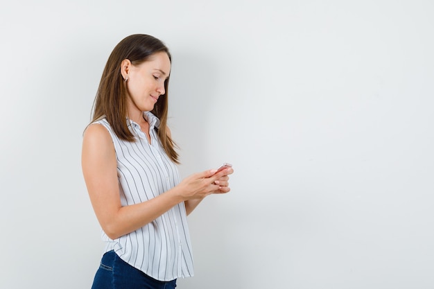 Chica joven con teléfono móvil y sonriendo en camiseta, vista frontal de jeans.