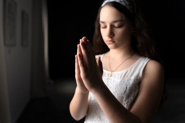 Chica joven de tiro medio rezando en el interior