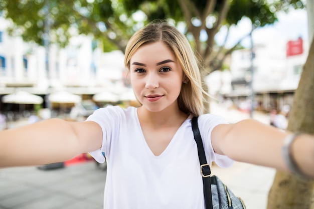 Chica joven toma selfie de manos con teléfono en la calle de la ciudad de verano.