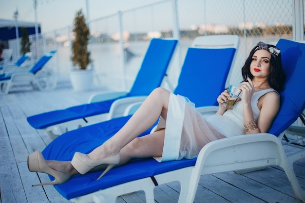Chica joven tomando una bebida mientras está tumbada en una hamaca azul