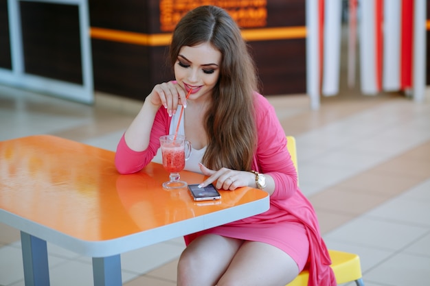 Chica joven tomando un refresco mientras mira su teléfono