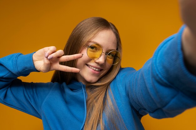 Chica joven tomando un selfie con gafas de sol y mostrando el signo de la paz