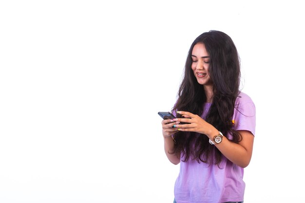 Chica joven tomando selfie o haciendo una videollamada en la pared blanca.