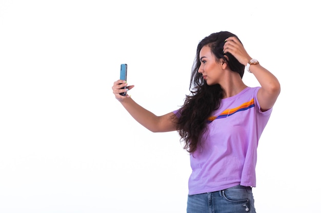 Chica joven tomando selfie o haciendo una videollamada y peinando su cabello.