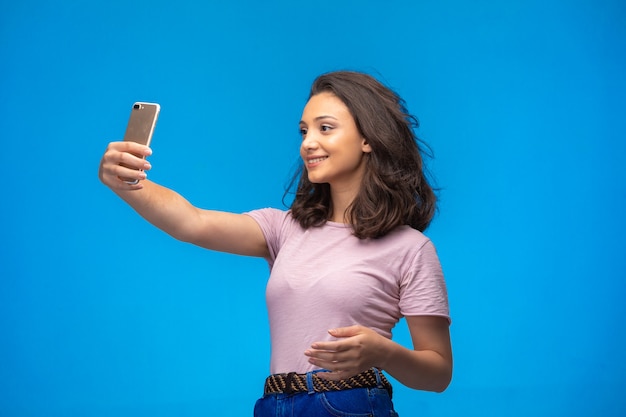 Chica joven tomando selfie con su teléfono inteligente y sonriendo.