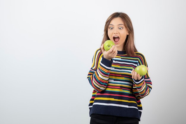 Chica joven en traje casual comiendo manzana verde sobre blanco.