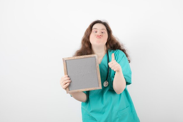 chica joven en uniforme verde con un marco que muestra un pulgar hacia arriba. mujer