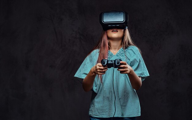 Chica joven vestida casual jugando el juego con el joystick y gafas de realidad virtual. Aislado en un fondo de textura oscura.