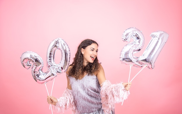 Chica joven vestida de forma festiva riendo sobre un fondo rosa con globos de navidad plateados para el concepto de año nuevo