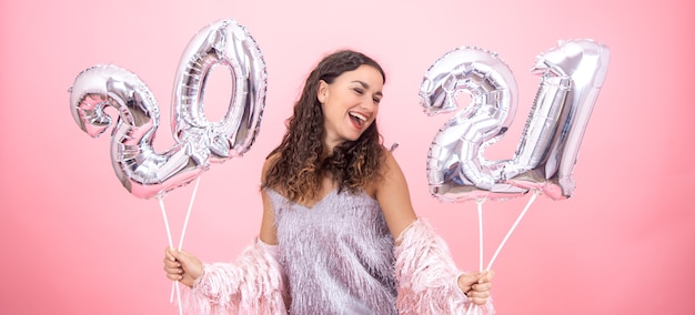 Chica joven vestida de forma festiva riendo sobre un fondo rosa con globos de navidad plateados para el concepto de año nuevo